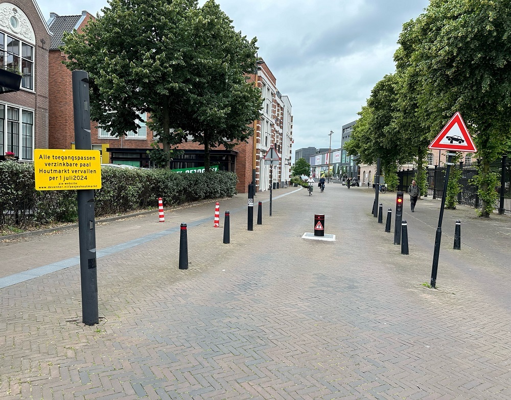 Straatbeeld met de paal en het nieuwe bord. Hierop staat: alle toegangspassen verzinkbare paal Houtmarkt vervallen per 1 juli 2024.